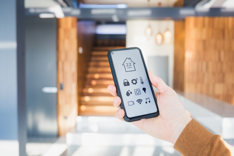 en hånd som viser frem en smarttelefon som viser oversikt over temperaturen i huset foran en trapp inne i huset.