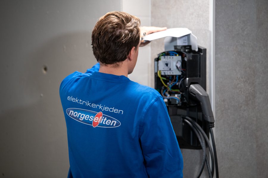 norgeselektriker står med ryggen til og holder på med en elbillader